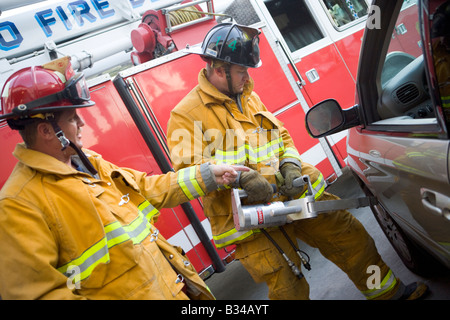 Zwei Feuerwehrmänner, die mit den Backen des Lebens auf einer Autotür Stockfoto