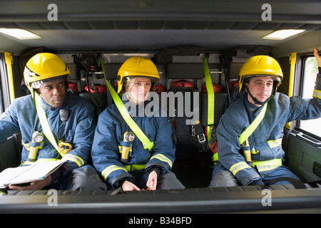 Drei Feuerwehrleute im Feuerwehrauto mit Helmen mit einer Lesung Stockfoto