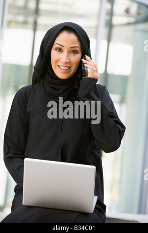 Geschäftsfrau, sitzen im Freien durch Gebäude mit Laptop mit Handy Telefon Lächeln auf den Lippen (Tiefenschärfe) Stockfoto