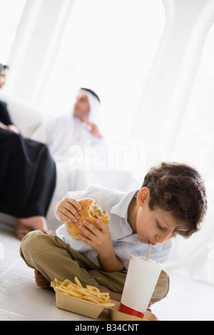 Junge mit Fast Food im Wohnzimmer mit den Eltern im Hintergrund (hohe Schlüssel/selektiven Fokus) Stockfoto