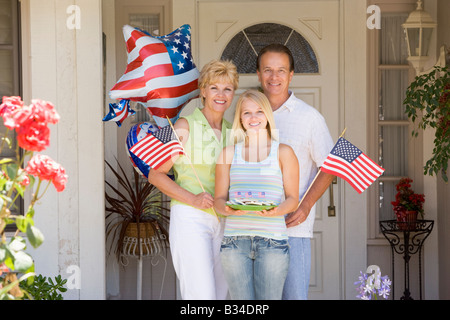 Familie an Haustür auf Fourth Of July mit Fahnen und Cookies lächelnd Stockfoto