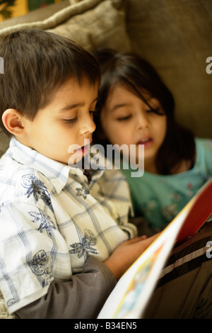 Jungen im Alter von sechs Jahren liest eine Geschichte um seine kleine Schwester im Alter von fünf Jahren Stockfoto