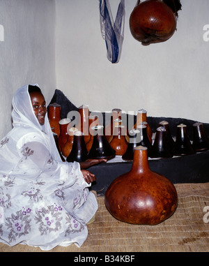 Uganda, Süd-Uganda, Mbarara. Ein Bahima Mädchen mit ihrer Familie aus Holz Milchtöpfe (bekannt als Ekyanzi) und Kürbisse, die einen besonderen angehobenen Schritt in einer Ecke des Wohnzimmers gehalten werden. Die Bahima sind Banyarwanda sprechende Menschen leben in der Nähe der Grenze von Ruanda in Süd-Uganda. Sie halten lange gehörnten Ankole Rinder, eine afrikanische Taurin Rasse mit Ursprung vor der Einschleppung der buckligen Rücken oder Zebu Rinder am Horn von Afrika während der menschlichen Invasionen aus Arabien im siebten Jahrhundert v. Chr. zurückgeht. Stockfoto