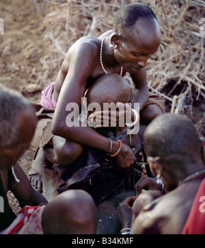 Kenya, Samburu District, South Horr. Samburu Jugendlicher ist außerhalb seiner Mutter Haus beschnitten, wie seine zwei Sponsoren besuchen ihn, ein Betrieb seine Schultern beim Drehen sein Gesicht weg von der Beschneider, der andere hält sein rechte Bein. Tropfen von Milch sind noch spürbar auf seinem Körper aus der Milch als Segen unmittelbar vor der Operation über den Kopf gegossen. Jungs dürfen keine Anzeichen von Angst oder Schmerz zu zeigen. Auch Nu ein Augenlid ist verpönt. Eine gute Beschneider dauert es eine Minute, um den Vorgang zu beenden, woraufhin brave Jungen Lebarta, die Samburu-Beschneidung-Lied singen. Stockfoto