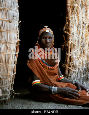 Kenia, Northern Frontier District Loyangalani. Ein Turkana-Frau sitzt in der Tür ihrer Hütte. Ihre schweren Mporro geflochtene Halskette identifiziert sie als verheiratete Frau. Typisch für ihren Stamm, trägt sie viele Schichten von Perlen Halsketten und Perlen Stirnband. Stockfoto