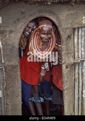 Kenia, Trans-Mara, Lolgorien. Maasai Mädchen in all ihrer Pracht und mit Glocken gebunden um ihre Beine warten am Eingang Stockfoto