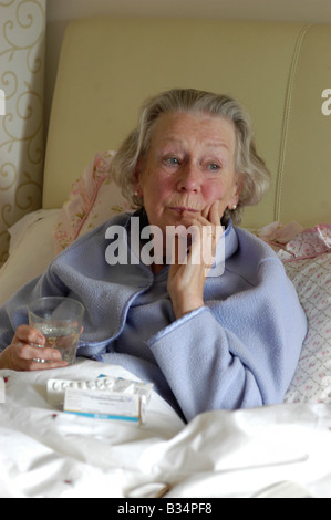alte Dame im Bett mit Pillen, die betroffenen suchen Stockfoto