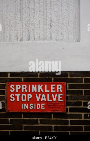 Sprinkler Ventil Stoppschild auf der äußeren Mauer eines Gebäudes unter einem weißen Teil der Wand. Stockfoto