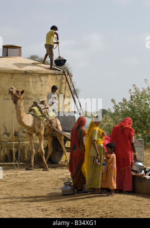 BANJARI STAMMESFRAUEN und Männer mit einem Kamel Wagen sammeln Wasser an ihren Brunnen in der THAR-Wüste in der Nähe von JAISALMER RAJASTHAN Indien Stockfoto