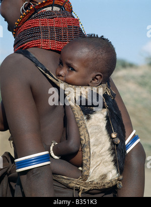 Kenia, Turkana, Nachola. Wenn eine Turkana Frau gebiert, werden in einem 24-Stunden-Zeitraum zur Feier des Tages vier Ziegen geschlachtet werden. Die Haut der erste Ziege erfolgt in einem Beutel für das Baby auf seiner Mutter Rücken zu tragen. Die kleine Holzkugeln auf der Rückseite der Tasche sind Reize um böse Geister abzuwehren. Das Baby trägt eine Armband von Strauß Eierschale Perlen. Stockfoto