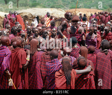 Kenia, Kajiado, Ilbisil. Eine bunte Sammlung von Maasai Krieger Sprung beobachten zwei ihrer Kameraden hoch in der Luft während eines Tanzes. Stockfoto