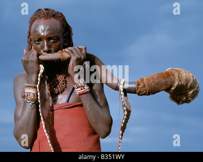 Kenia, Trans-Mara, Lolgorien. Ein Massai-Krieger bläst eine Trompete aus dem Horn eine große Kudu umgearbeitet. Der Gurt ist mit Kaurimuscheln verziert. Kudu-Horn-Trompeten sind nur Klang, um Männer zu den Waffen oder bei feierlichen Anlässen zu nennen. Stockfoto