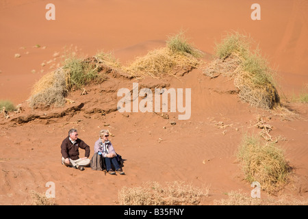 Ein Mann und eine Frau sitzen unter Sanddünen von Sossusvlei Düne Gegend im Süden Namibias in Namib-Naukluft-Park in Afrika Stockfoto