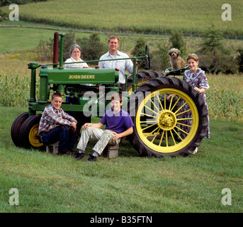 Bauernhof-Ausrüstung-Mechaniker und seine Familie posieren mit einem antiken John Deere Traktor. Stockfoto