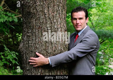 Ein Geschäftsmann im Anzug umarmt einen Baum, Treehugger corporate Umweltschutz darstellt Stockfoto