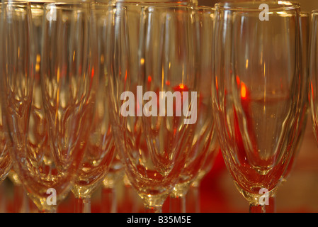 Eine Reihe von Zeilen mit leeren Sektgläser, bei einer Hochzeitsfeier mit roter Beleuchtung hinter ihnen. Stockfoto