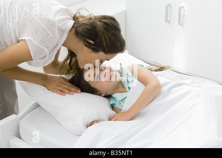 Mädchen im Bett liegend, Mutter biegen über ihre Stirn küssen Stockfoto