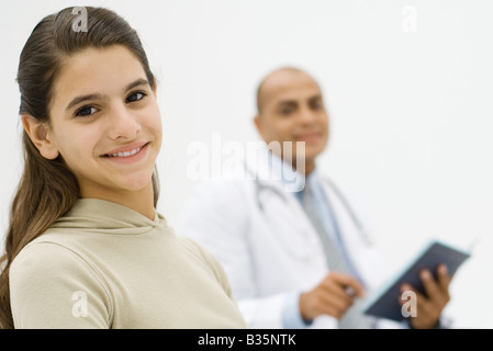 Teenager-Mädchen lächelnd in die Kamera, Arzt hält Ordner im Hintergrund Stockfoto