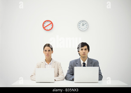 Büroangestellte sitzen unter Uhren, mit Laptops, Warnung melden Sie über eine Uhr Stockfoto