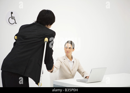 Berufstätige Frau Händeschütteln mit Mann auf Krücken Stockfoto