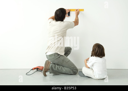 Mann Mess Wand mit einem Lineal während seines Sohnes Uhren, Bohren Sie auf dem Boden in der Nähe Stockfoto