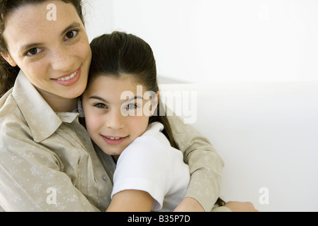 Junge Frau und Mädchen umarmen einander, lächelnd in die Kamera, Porträt Stockfoto