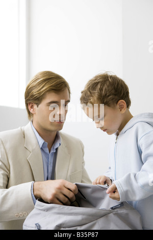 Gut gekleideter Mann kauert nach unten, halten Rucksack zusammen mit seinem Sohn Stockfoto