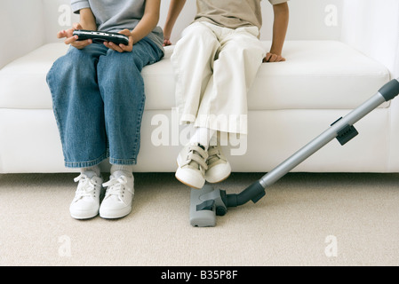 Zwei Kinder sitzen auf Sofa als übergeordnete Staubsauger, einem handheld Videospiel Ansicht beschnitten Stockfoto