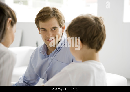 Familie sitzen zusammen auf Vater lächelnd an jungen Sohn konzentriert Stockfoto