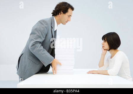 Geschäftsmann, hohen Stapel von Papier über eine Tabelle zu Frau stützte sich auf ihre Ellbogen gleiten Stockfoto