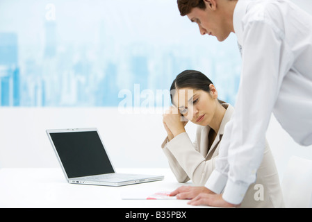 Frau auf der Suche nach unten und hielt Kopf, Kollege am Schreibtisch gelehnt und über die Schulter schauen Stockfoto