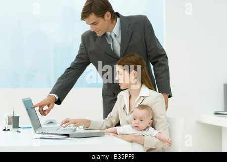 Berufstätige Frau im Büro mit Baby auf Schoß, Blick auf Laptop mit männlichen Kollegen Stockfoto