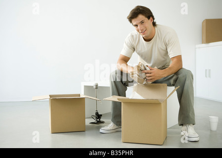 Mann Auspacken Boxen, sitzen auf Bank, lächelnd in die Kamera Stockfoto