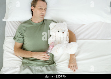 Vater schlafend im Bett, hält Babyflasche und Teddybär, Draufsicht Stockfoto