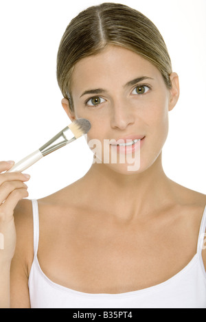 In die Kamera lächelnde Frau auftragen Gesicht Puder mit einem Make-up-Pinsel Stockfoto