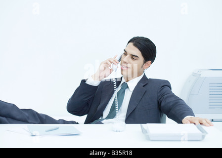 Junger Geschäftsmann mit Füßen sitzend am Schreibtisch, Festnetz telefonieren Stockfoto