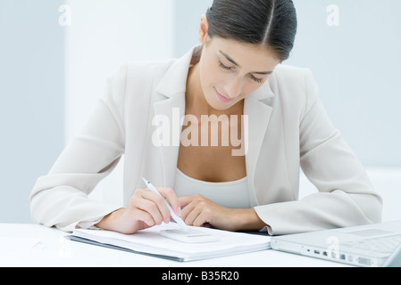 Junge Geschäftsfrau mit Stift Zahlen auf Rechner, auf der Suche nach unten eingeben Stockfoto