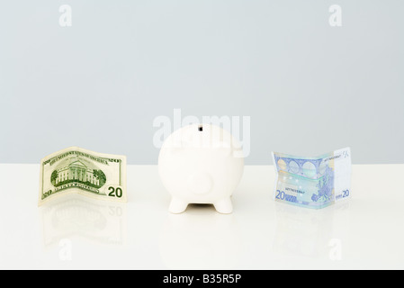 Sparschwein mit gefalteten zwanzig Dollarschein auf der einen Seite und ein 20 Euro-Schein auf der anderen Seite Stockfoto