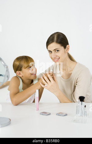 Preteen Mädchen putting Make-up auf ihre ältere Schwester, junge Frau lächelt in die Kamera Stockfoto