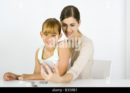 Mädchen sitzen auf junge Frau Schoß, Blick in den Handspiegel zusammen Stockfoto