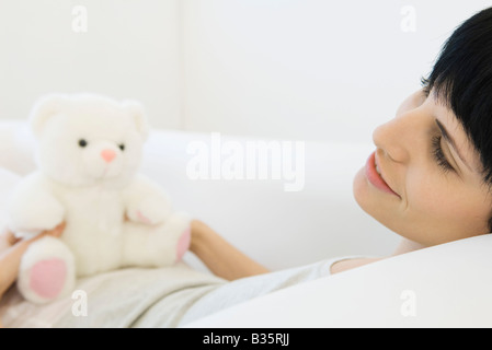 Frau auf Rücken auf Sofa, Teddybär sitzend auf dem Bauch liegend wegschauen Stockfoto