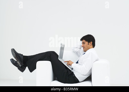 Gut gekleideter Mann im Sessel zurücklehnen, mit Laptop, Seitenansicht Stockfoto