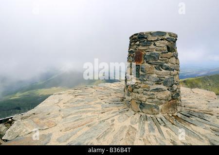 Der Cairn der Gipfel des Mount Snowdon mit schweren Wolken hängen über dem Tal weit unten Stockfoto