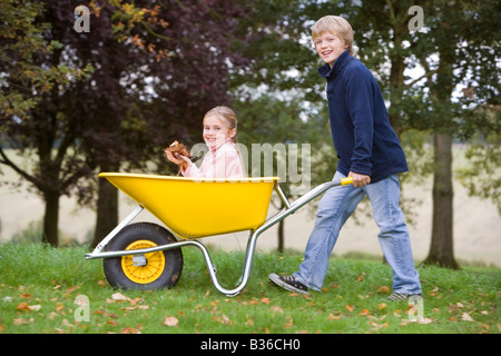 Junge im freien drängen junge Mädchen in Schubkarren und lächelnd (Tiefenschärfe) Stockfoto