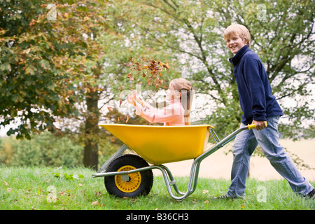 Junge im freien drängen junge Mädchen in Schubkarren und lächelnd (Tiefenschärfe) Stockfoto