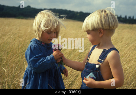 kleiner Junge die kleinen Mädchen eine Reihe von wilden Blumen in einem Feld von Mais Stockfoto