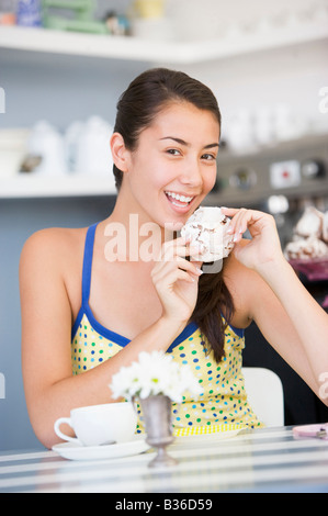 Junge Frau sitzt an einem Tisch essen eine süße Leckerei Stockfoto