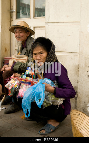 Eine alte vietnamesische Frau starrt auf den Betrachter beim hocken auf dem Bürgersteig in der alten Viertel von Hanoi-Vietnam Stockfoto