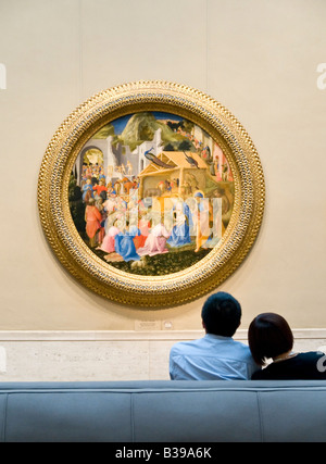 WASHINGTON DC, USA – Ein Paar sitzt auf einer Bank und bewundert das Gemälde „Anbetung der Könige“ von Fra Angelico und Filippo Lippi, ca. 1440–1460, das in der National Gallery of Art in Washington DC ausgestellt ist. Das Renaissance-Kunstwerk zeigt die biblische Szene der drei Könige, die dem Kleinkind Jesus Geschenke überreichen. Stockfoto