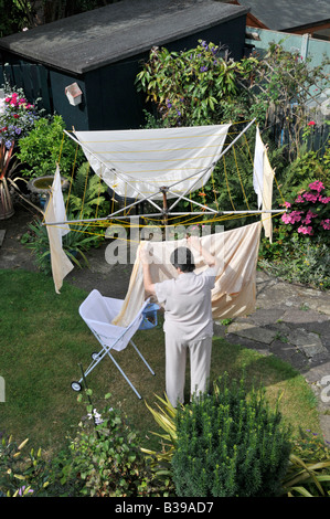 Luftaufnahme der Hausfrau Frau, die aus dem Haushaltsbett peggt Leinentausch zum Trocknen auf rotierender Wäscheleine im Haushalt Back Garden Essex England Großbritannien Stockfoto